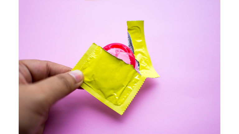 Close-Up Of Man Holding Condom Over Pink Background