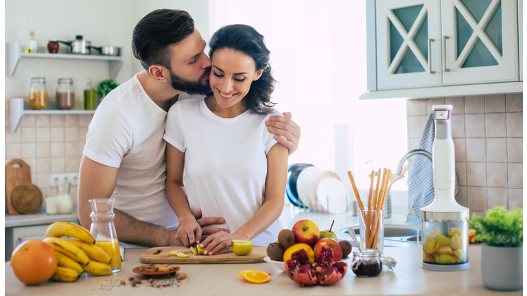 Excited happy beautiful young couple in love cooking in the kitchen and having fun together while making fresh healthy fruits salad
