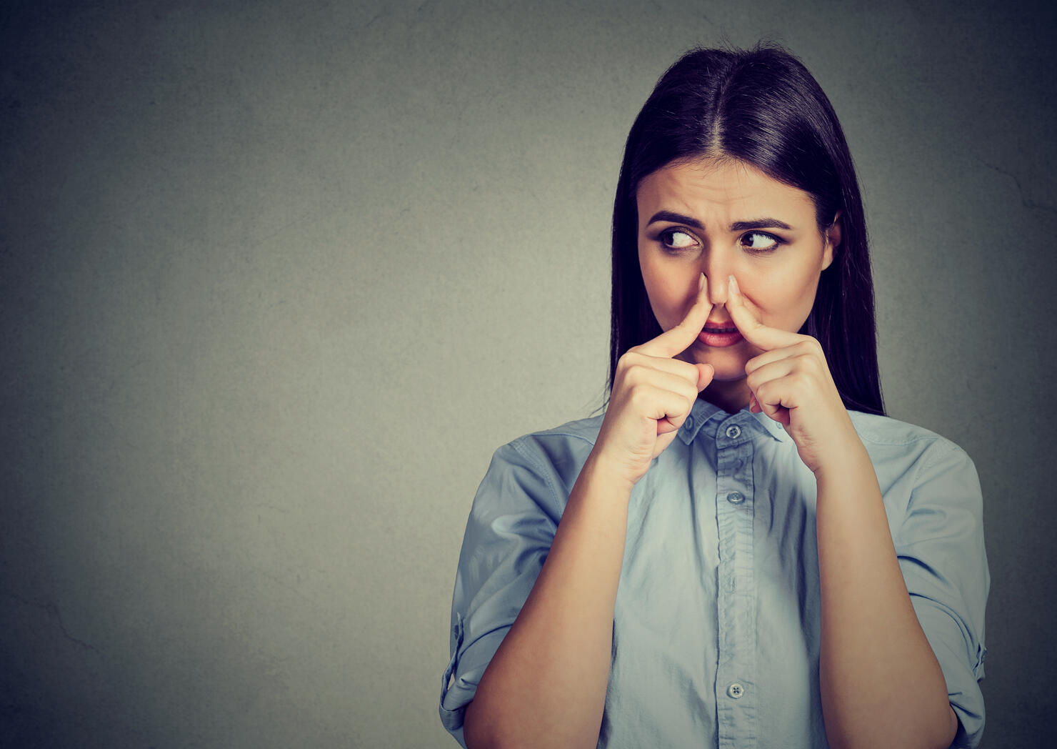 Woman pinches nose with fingers looks with disgust away something stinks bad smell