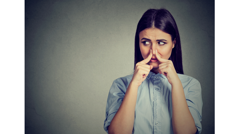 Woman pinches nose with fingers looks with disgust away something stinks bad smell