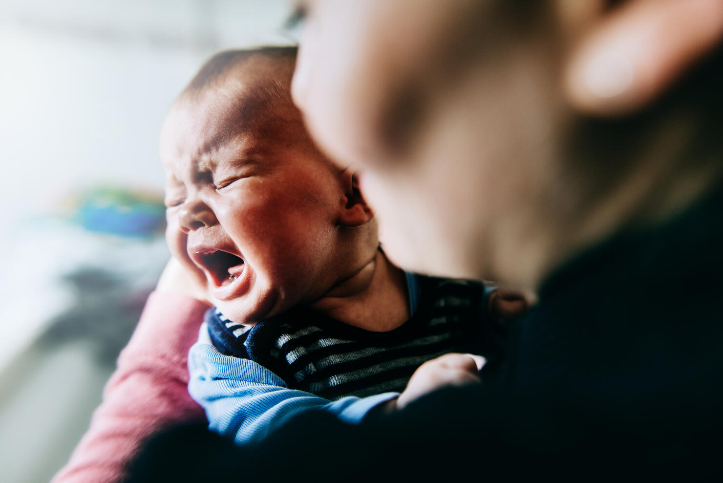 Baby girl holding by mother crying out loud.