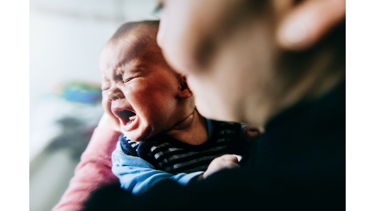Baby girl holding by mother crying out loud.