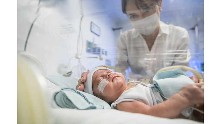 Loving mother looking at her newborn in an incubator while wearing a facemask