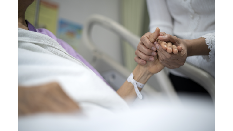 Shot of daughter encourage her mother and holding the mother's hand to sleep on the bed ​in hospital.