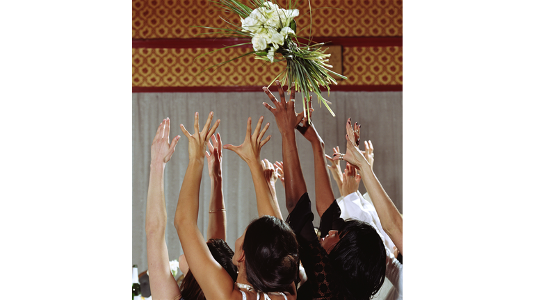 Women at wedding reception reaching to catch bouquet, high section