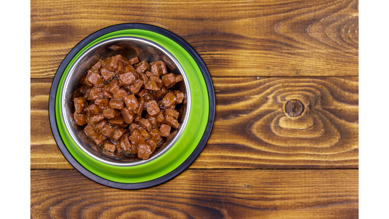 Canned food for cats or dogs in green metal bowl on wooden floor. Top view