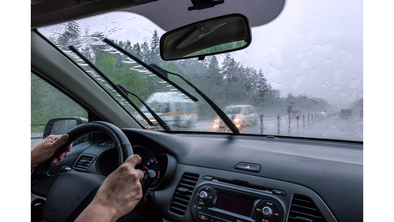 View through the rain-drenched windshield. Driver's hands and part of the car interior