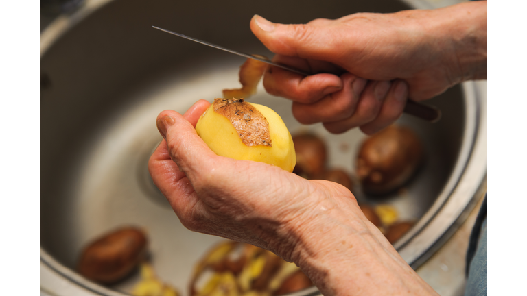 Elderly woman to peel potatoes. Kitchen working. Prepare food