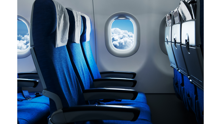 Empty air plane seats. Blue sky and clouds in the window. Airplane interior