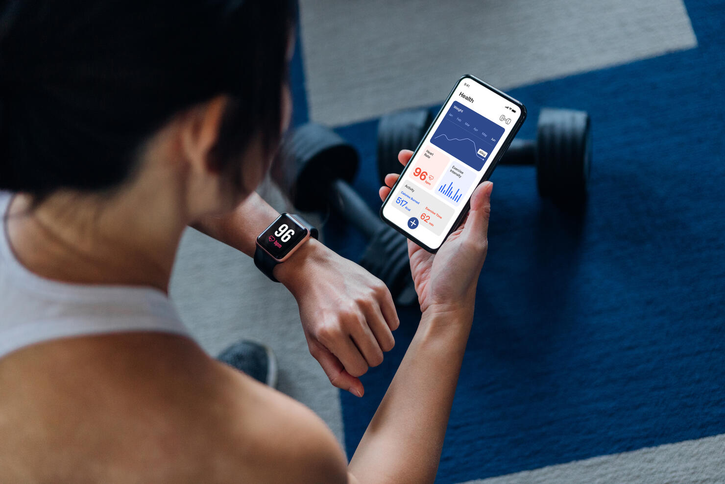 Over the shoulder view of young active woman using exercise tracking app on smartphone to monitor her training progress after exercising at home