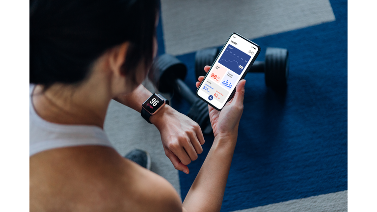 Over the shoulder view of young active woman using exercise tracking app on smartphone to monitor her training progress after exercising at home