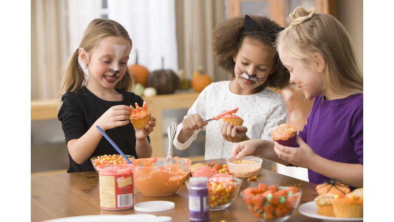 Girls in Halloween costumes decorating cupcakes