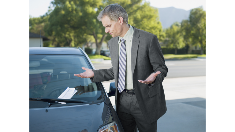 Frustrated businessman viewing parking ticket on windshield