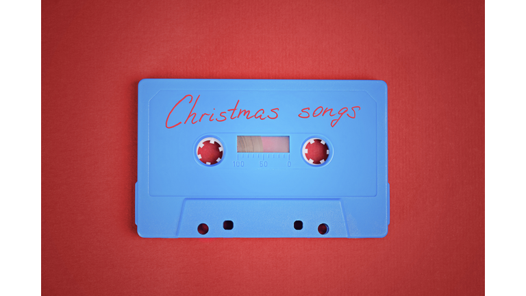 Blue audio cassette tape with christmas songs laying on red paper background.