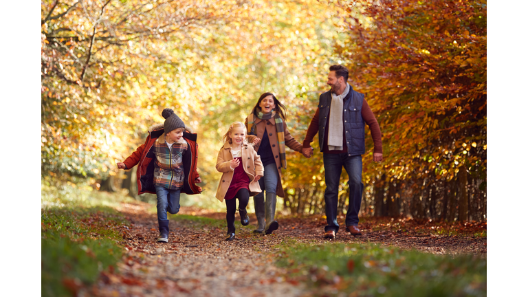 Family Walking Along Track In Autumn Countryside With Children Running Ahead