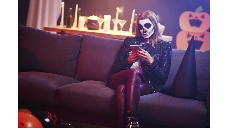 Bored woman using mobile phone at Halloween party