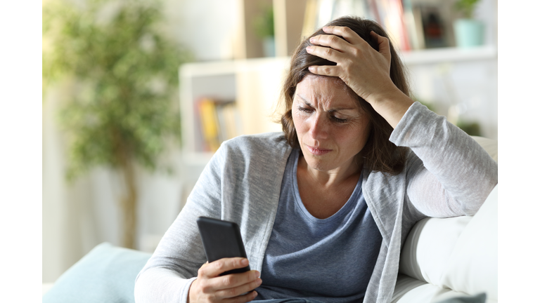 Sad adult woman reading news on phone at home