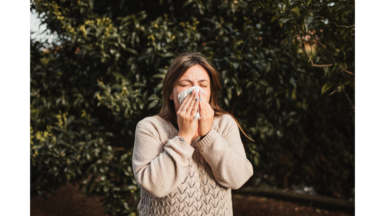 young woman suffering spring allergy and blowing nose with a tissue in the nature