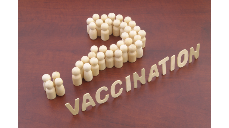 People (wooden figures) shaped as question mark and word vaccination.