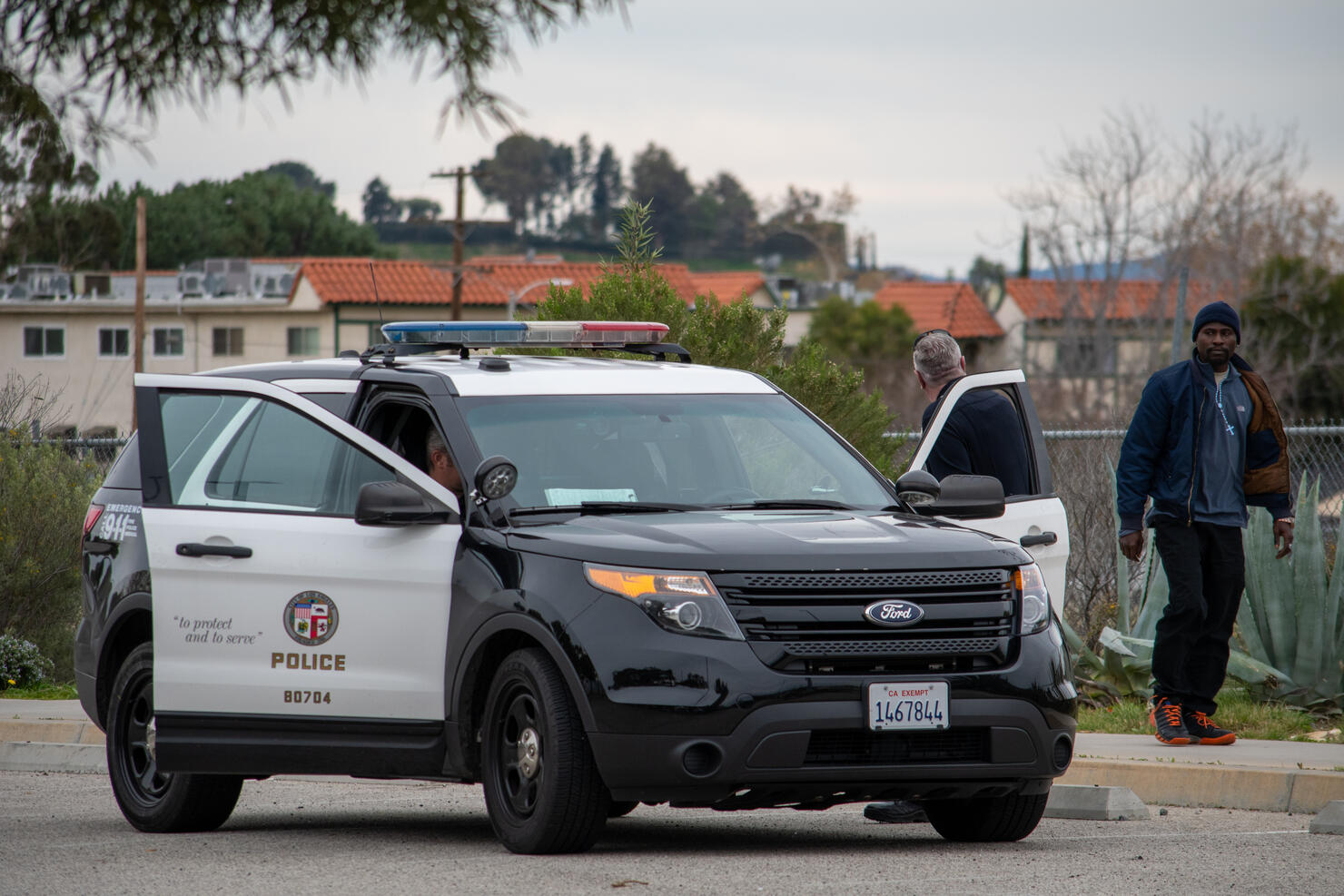 LAPD officers conduct an assault investigation at 10040 Old Depot Plaza Rd, at the Chatsworth Train Station, as a pedestrian walks by.