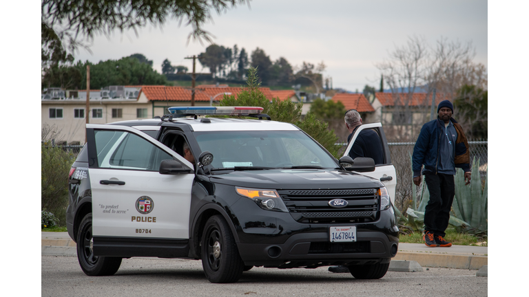 LAPD officers conduct an assault investigation at 10040 Old Depot Plaza Rd, at the Chatsworth Train Station, as a pedestrian walks by.