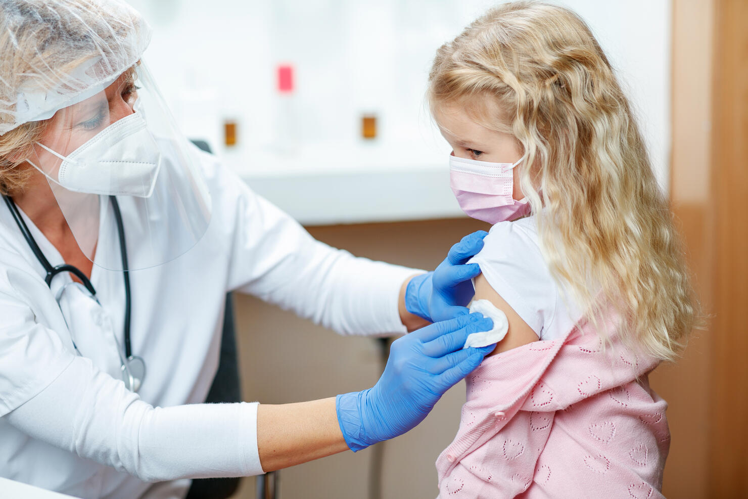 Female doctor cleaning girl's arm with cotton pad before COVID-19 vaccination