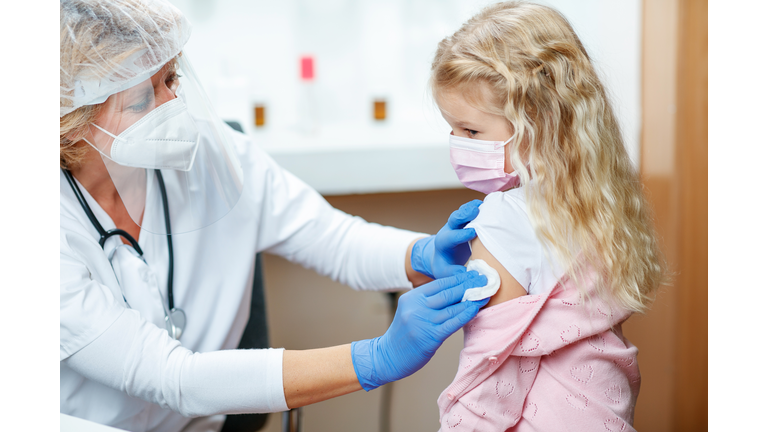 Female doctor cleaning girl's arm with cotton pad before COVID-19 vaccination