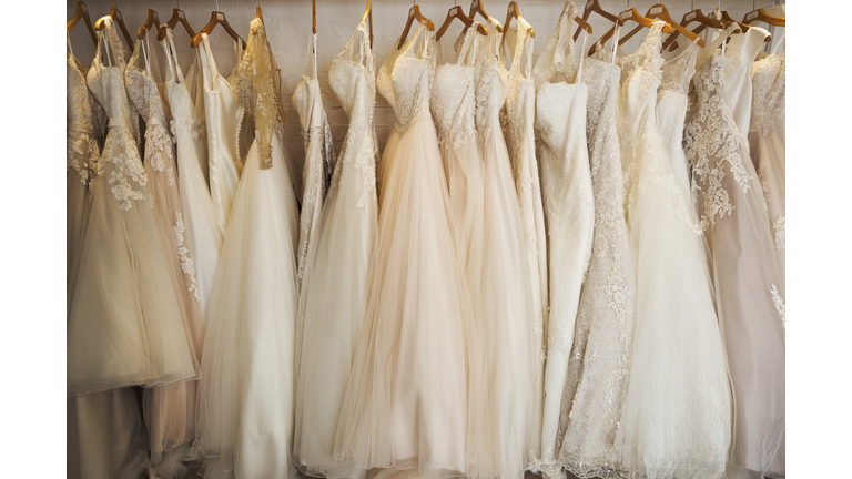 Rows of wedding dresses on display in a specialist wedding dress shop. A variety of colour tones and styles, fashionable lace and boned bodices. 