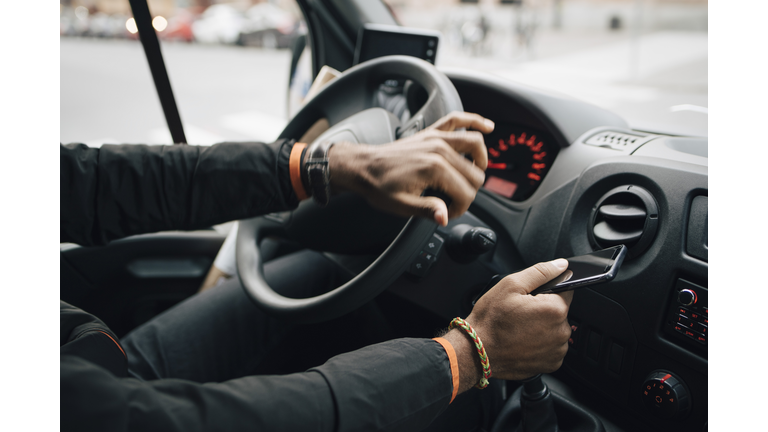 Cropped image of man holding mobile phone while driving delivery van