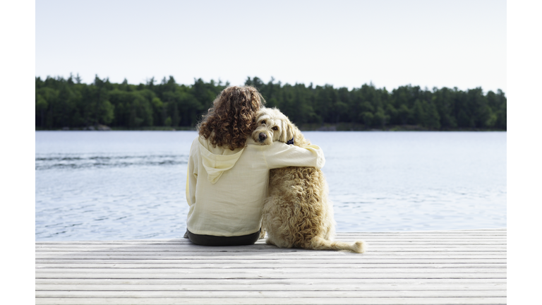 Woman sitting with dog on jetty, rear view