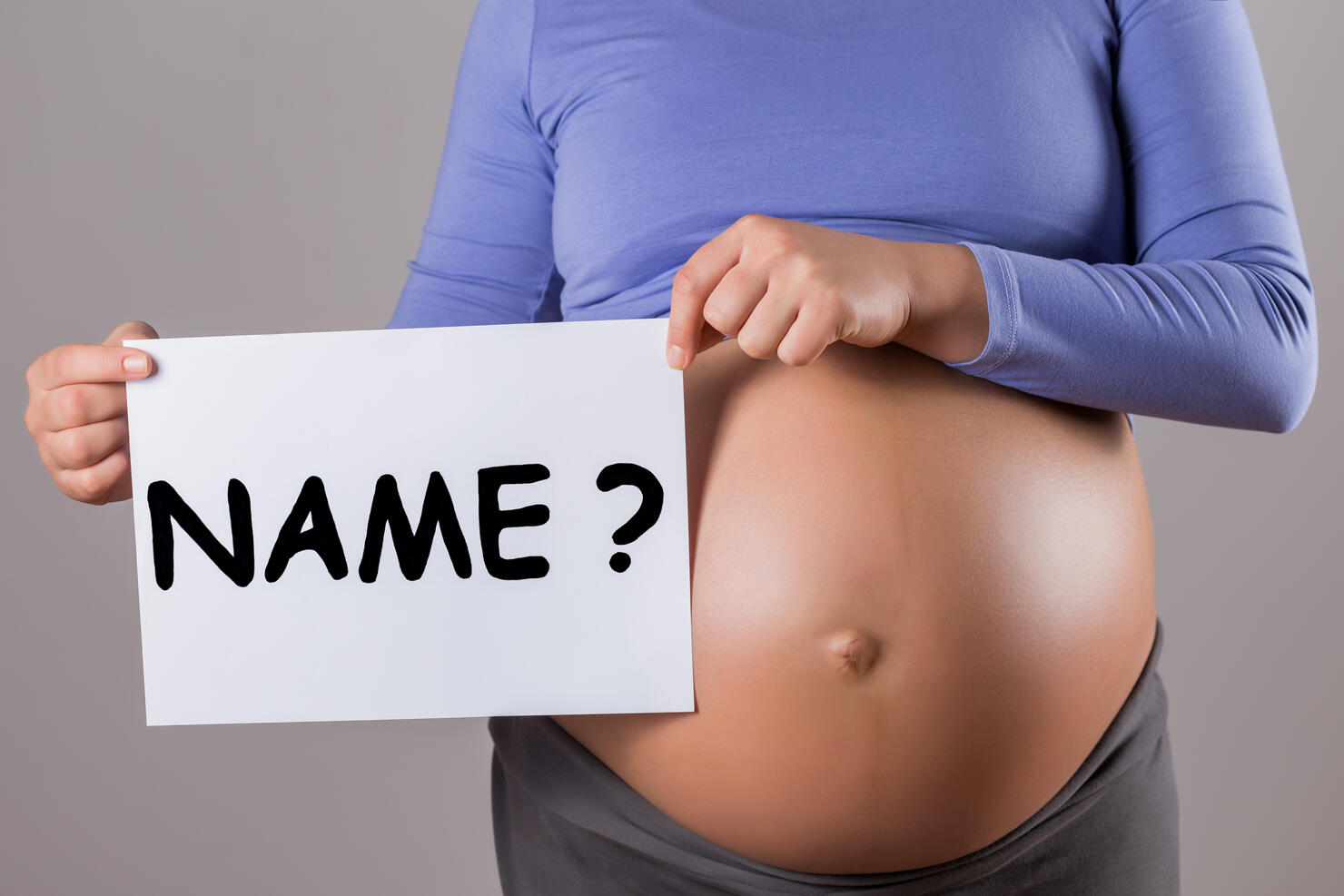 Stomach of pregnant woman holding paper with question name