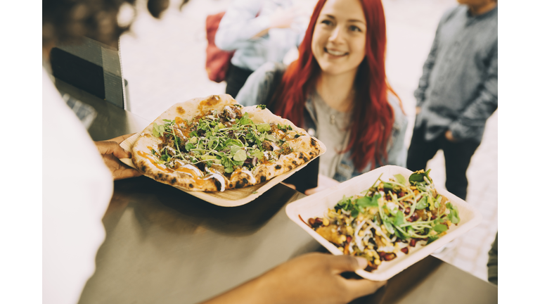 Female assistant giving food plate to smiling female customer in city