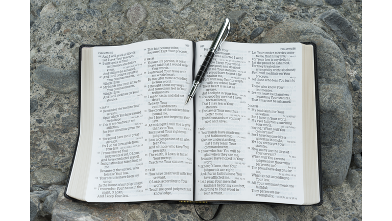 Open bible in Psalm 119 with a fountain pen. Stone background.