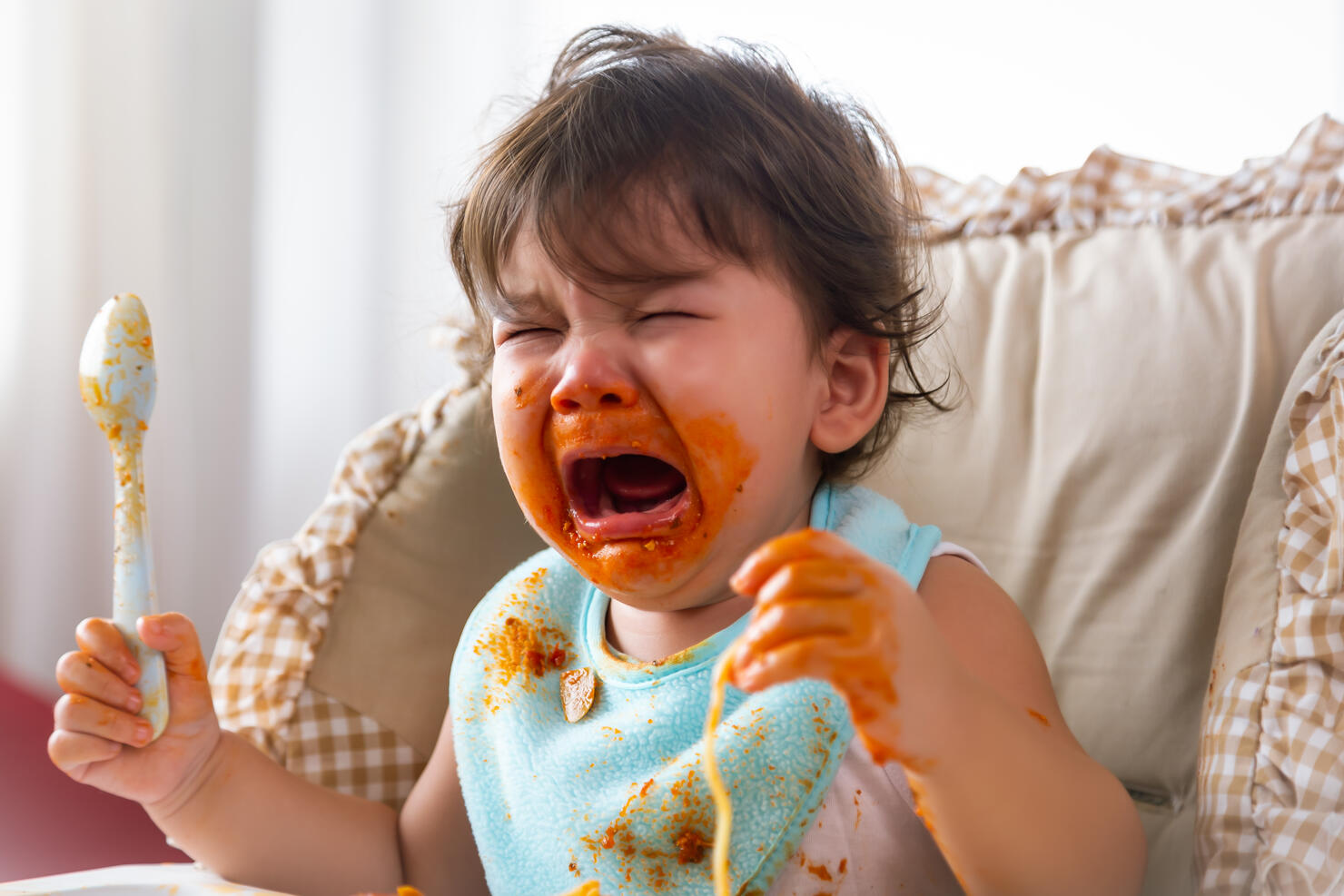 Adorable little toddler girl or infant baby crying when unsatisfied when finished eating food on baby chair. Cute infant girl get hungry and want more food. Mix race daughter get dirty Kid get tantrum