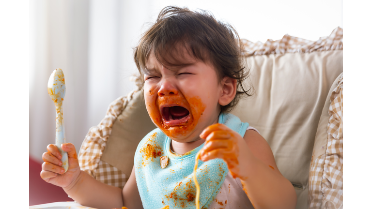 Adorable little toddler girl or infant baby crying when unsatisfied when finished eating food on baby chair. Cute infant girl get hungry and want more food. Mix race daughter get dirty Kid get tantrum