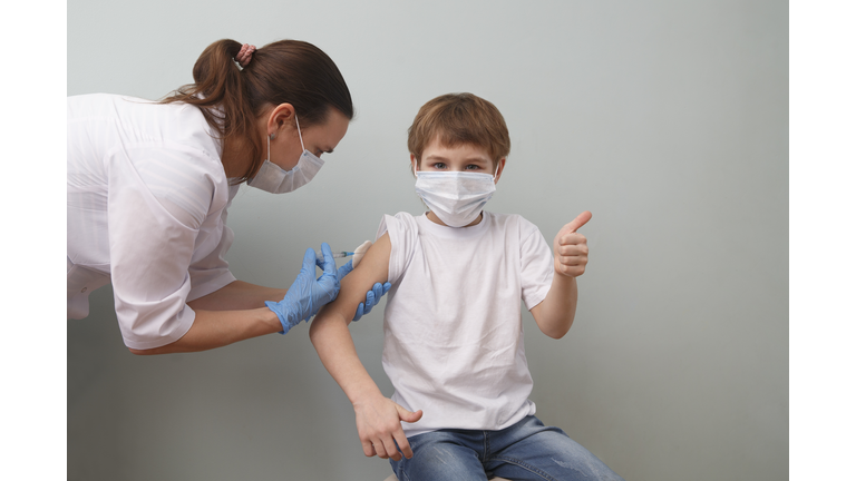 Pediatrician wearing a protective face masks makes vaccination to cute caucasian schoolboy in clinic.
child boy show sight thumbs up during vaccination