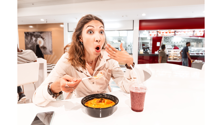 A woman eating too hot and peppery soup in an Asian fast food restaurant. Concept of spices in Oriental cuisine