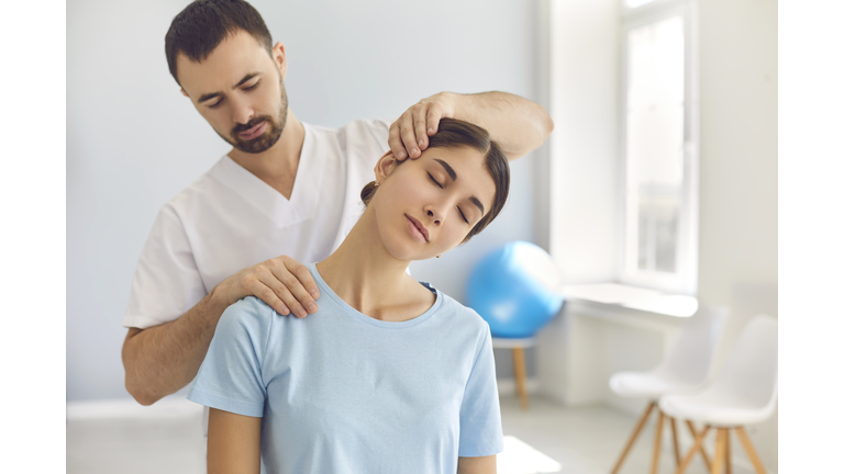 Licensed chiropractor doing neck adjustment to female patient in modern medical office