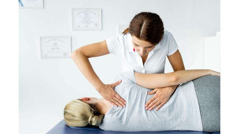 attractive chiropractor touching hand of patient in grey t-shirt