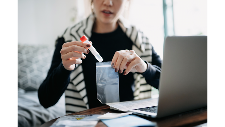 Cropped shot of young Asian woman consulting to her family doctor online in a virtual appointment, holding a medical test tube, conducting Covid-19 diagnostic test at home