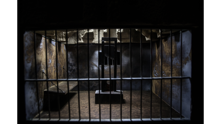 Jail or prison cell. Obsolete gray grunge concrete room. Creative artwork decoration. Horror view of Guillotine scale model in the dark