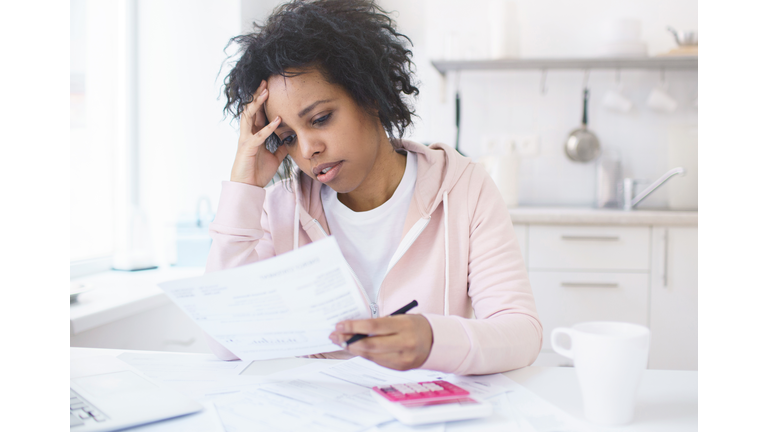 Upset african american woman sitting at kitchen table with laptop, dealing with financial stress and pressure because of mortgage debt, worrying or feeling anxious. No money concept