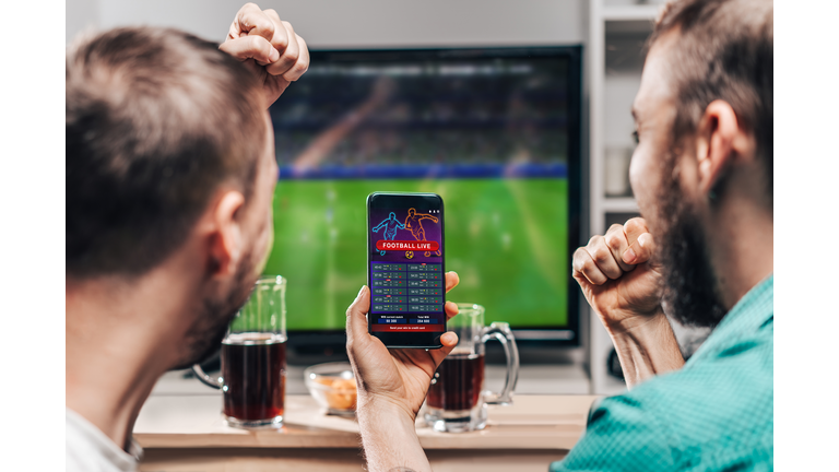 Two male friends watching live football game broadcast on tv