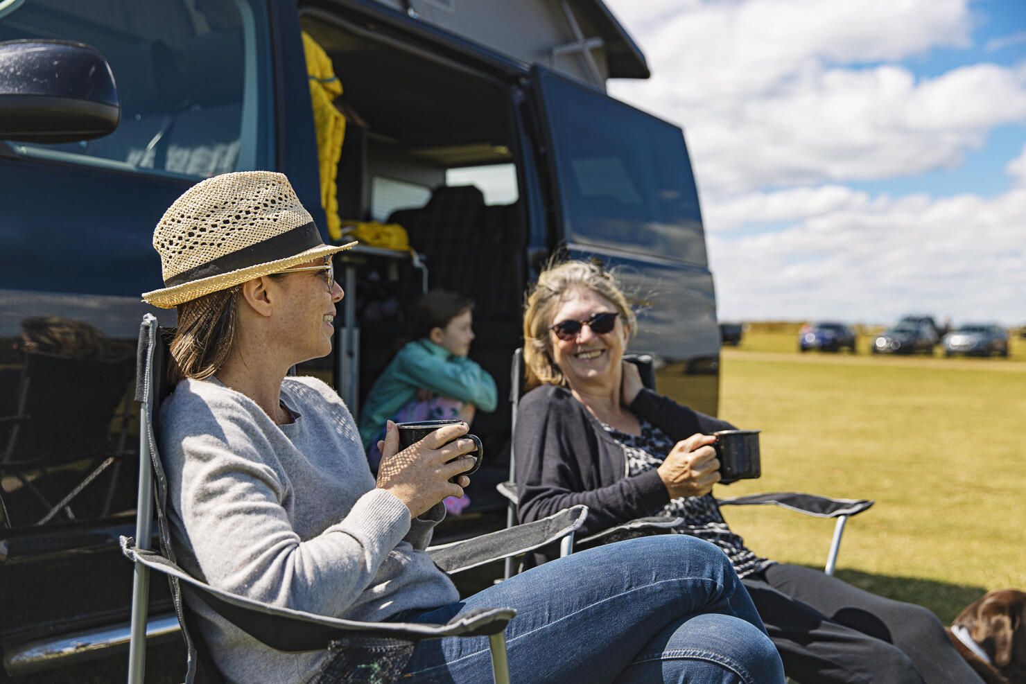 Woman having a cuppa by the camper van with her mother and daughter