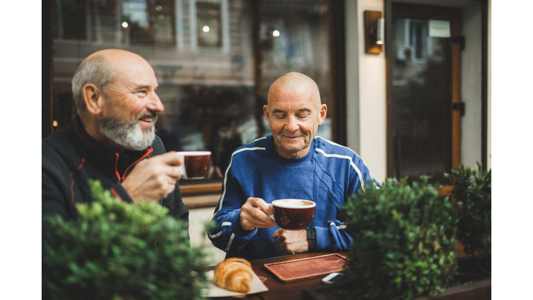 Two old age senior friends drinking coffee in cafe on outside terrace. Laughing and talking. Young at heart