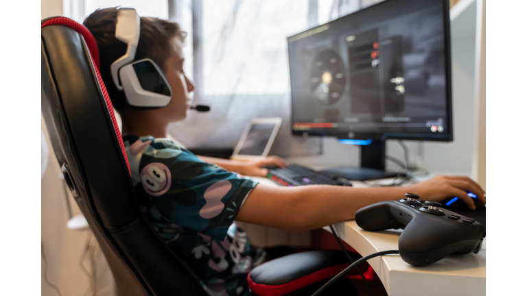 Selective focus on a remote control next to a teenager sitting in an armchair in front of a computer playing with the mouse while wearing helmets . Gaming concept