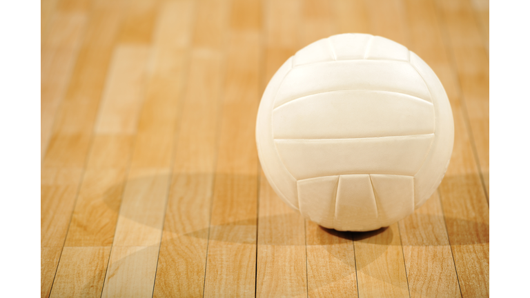 A lone white volleyball sitting on a wooden floor