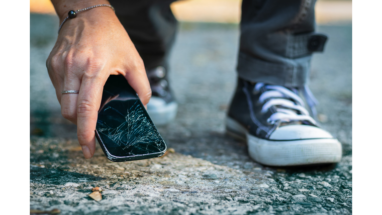 Woman picking up broken smartphone from the ground.