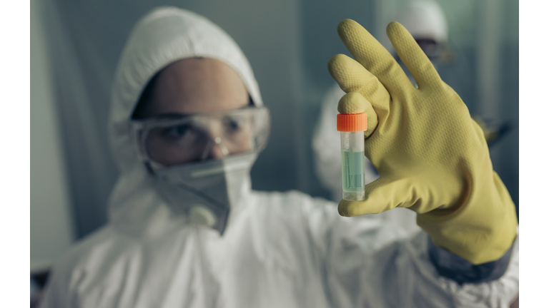 Woman with baceriological protective suit looking at an antidote vial