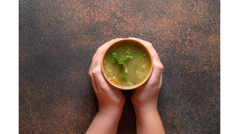 Chicken broth with greens in craft paper containers in child hand. Soup to go, healthy food delivery. View from above.